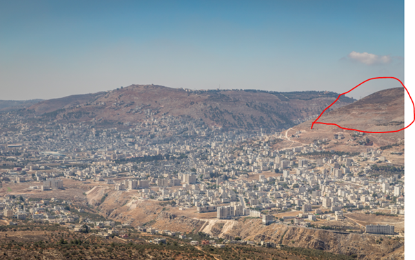 Mount Ebal (in Red circle). To its left is biblical Mount Gerizim (mountain of blessings). The large city in the valley is Nablus (biblical Shechem). For those who are unable to arrange an IDF escort to Mount Ebal itself, the next best way to experience these Biblical sites safely is from the Jewish settlement of Elon Moreh (where this picture was taken). Photo Credit: alefbet / Shutterstock